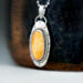 3/4 left view hanging on black pot, oval orange stone bezel set accented with twisted wire and a stamped base, diamond cut chain